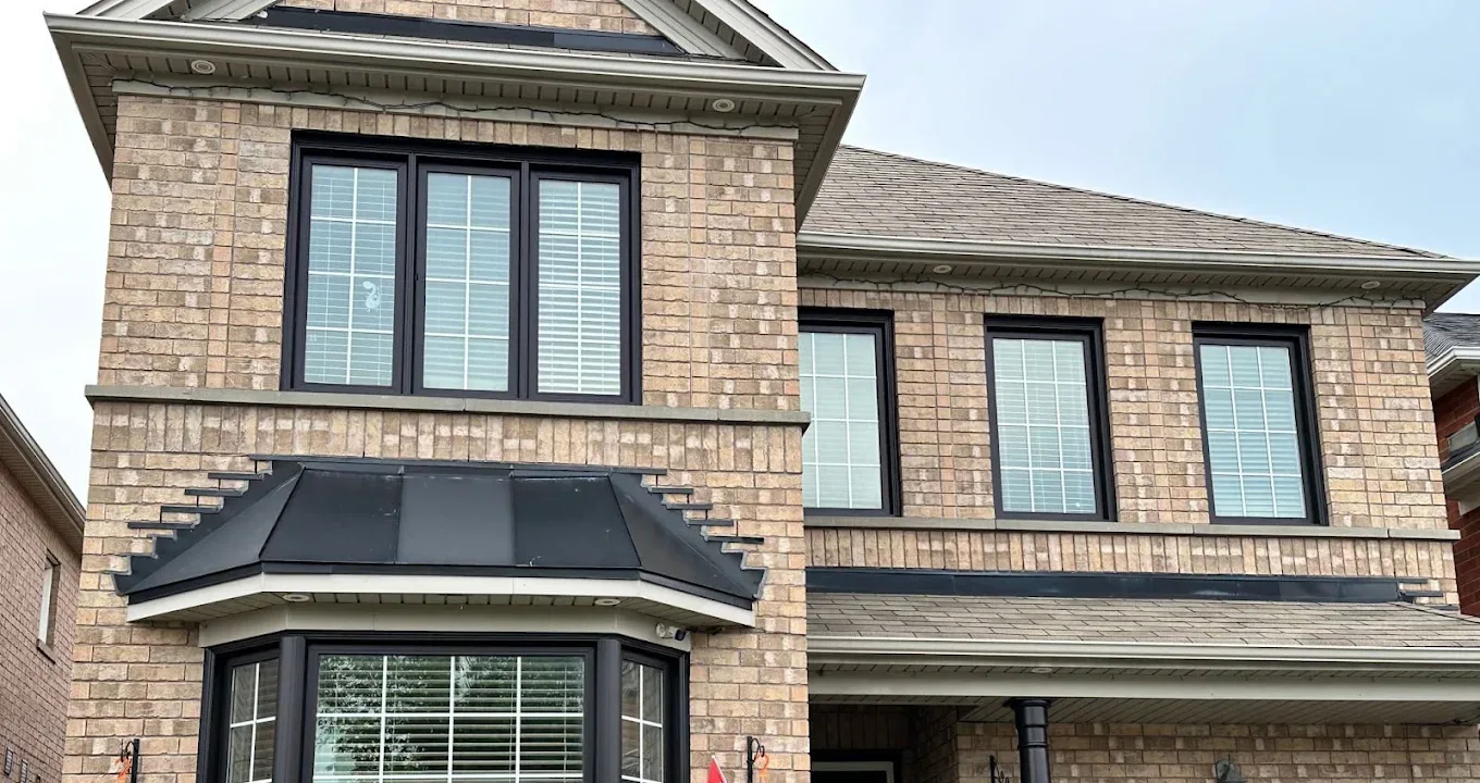 Brick home exterior with freshly finished dark window and roof trim